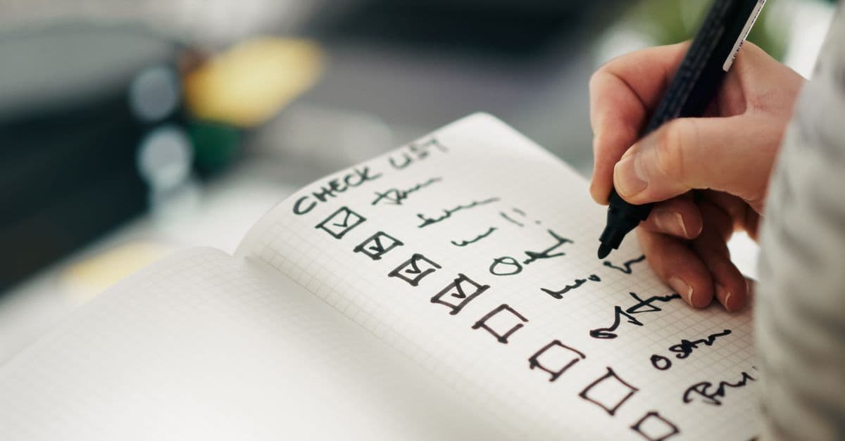 Hand schreibt Aufgaben auf eine Checkliste, Fokus auf Planung und Organisation