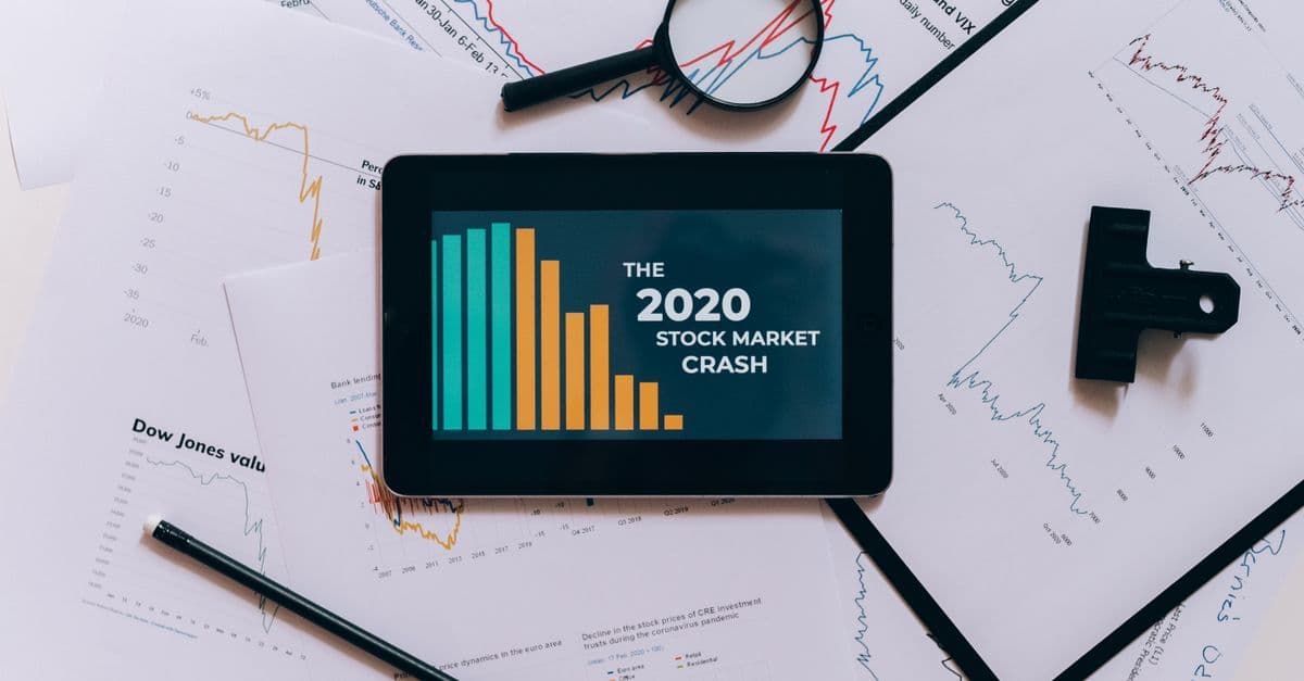 Tablet mit Börsencharts zum Crash 2020 neben ausgedruckten Diagrammen im Flatlay