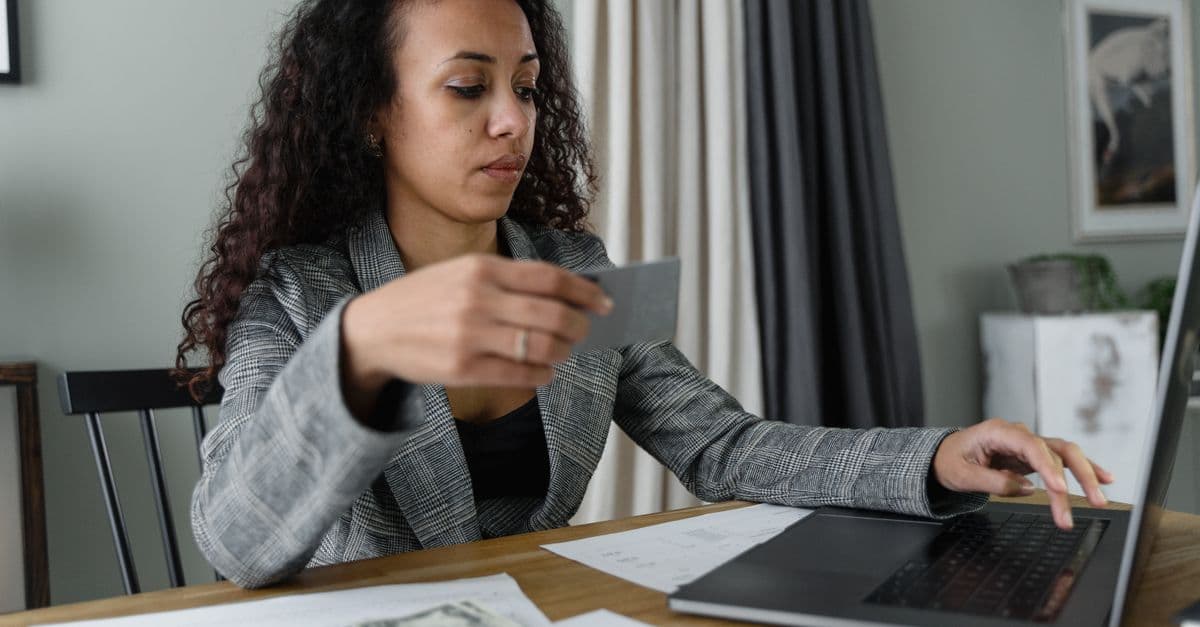 Frau verwaltet Finanzen am Laptop, mit Bargeld und Bankkarte auf Holztisch in Innenraum.
