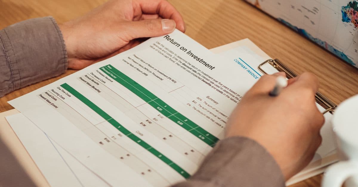 Person analysiert mit einem Stift einen Renditebericht am Schreibtisch.