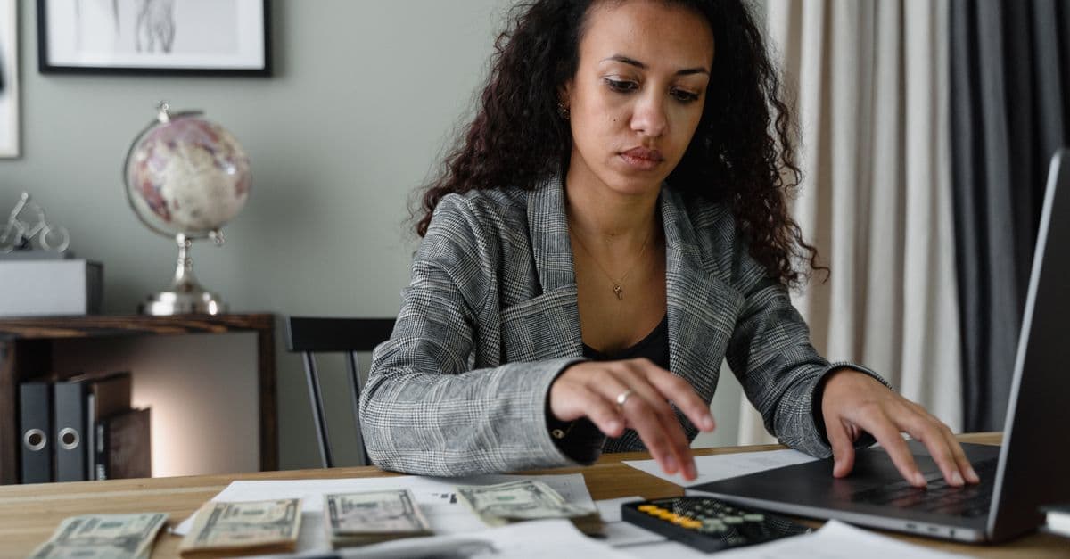 Berufstätige Frau prüft Finanzunterlagen und zählt Bargeld am Schreibtisch im Büro.